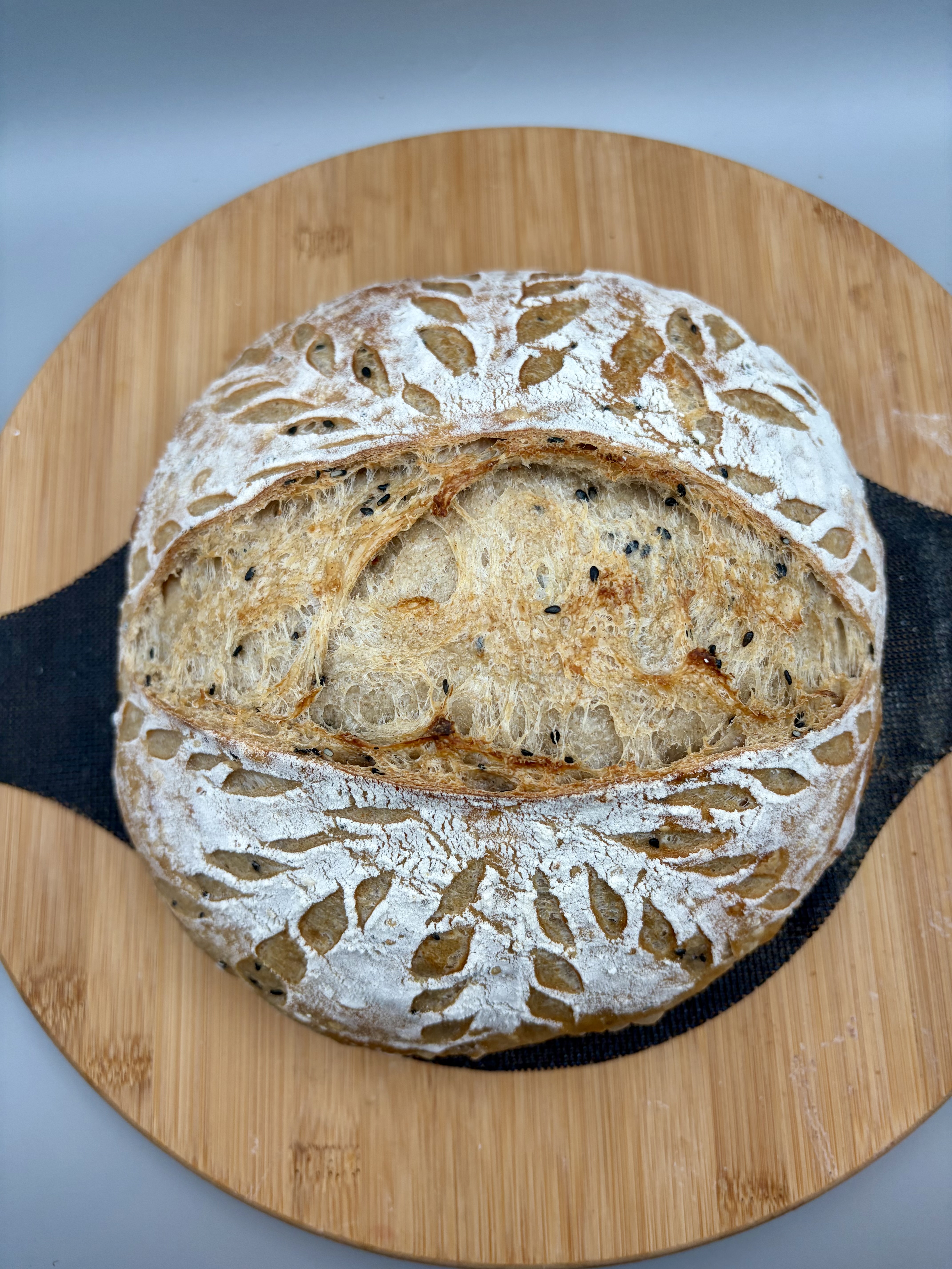 Top-down view of the poppy seed boule on a bamboo board, leaf-pattern scoring fully open